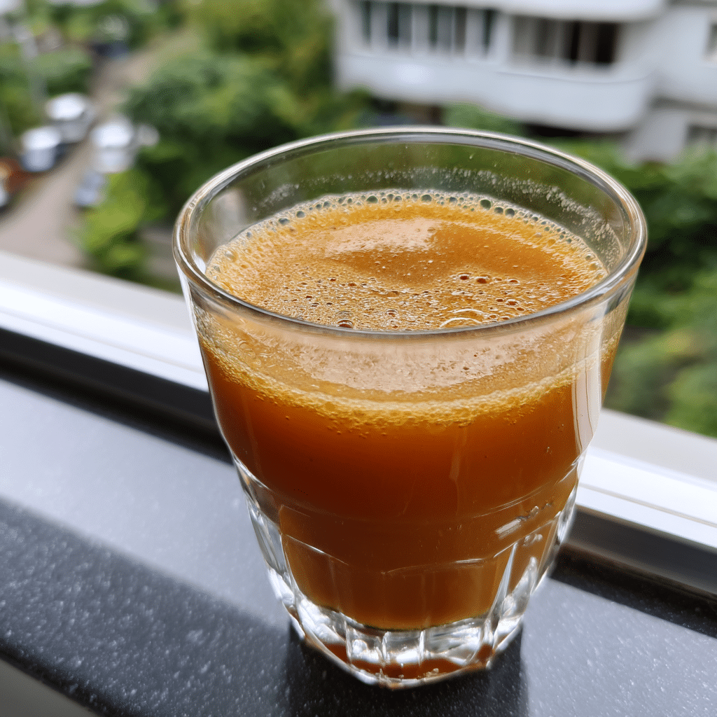 Glass of freshly made Natural Mounjaro Recipe detox drink with a rich orange hue, placed on a windowsill.
